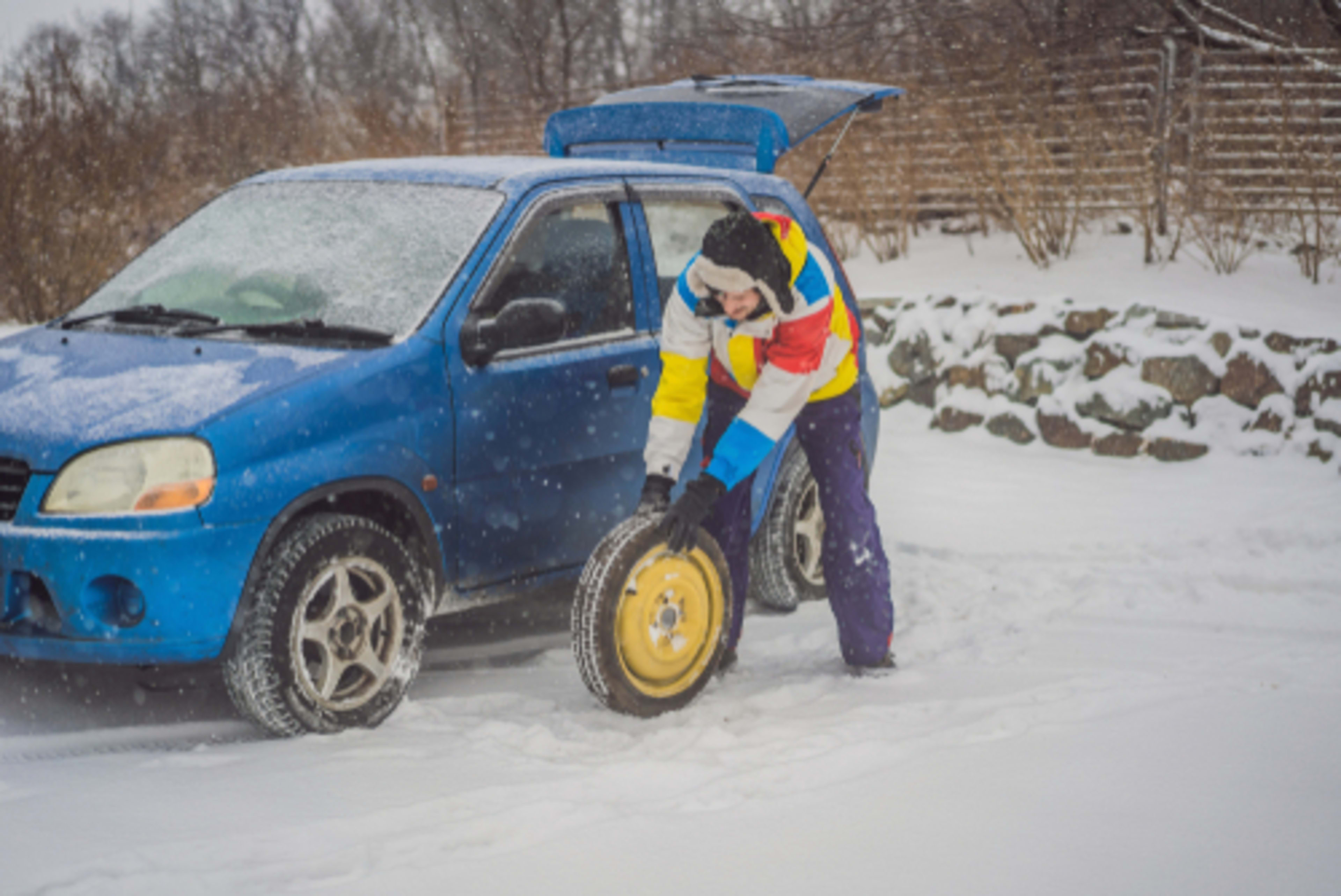 Rolling a car's spare tire up to the flat tire to change it out, while it snows.