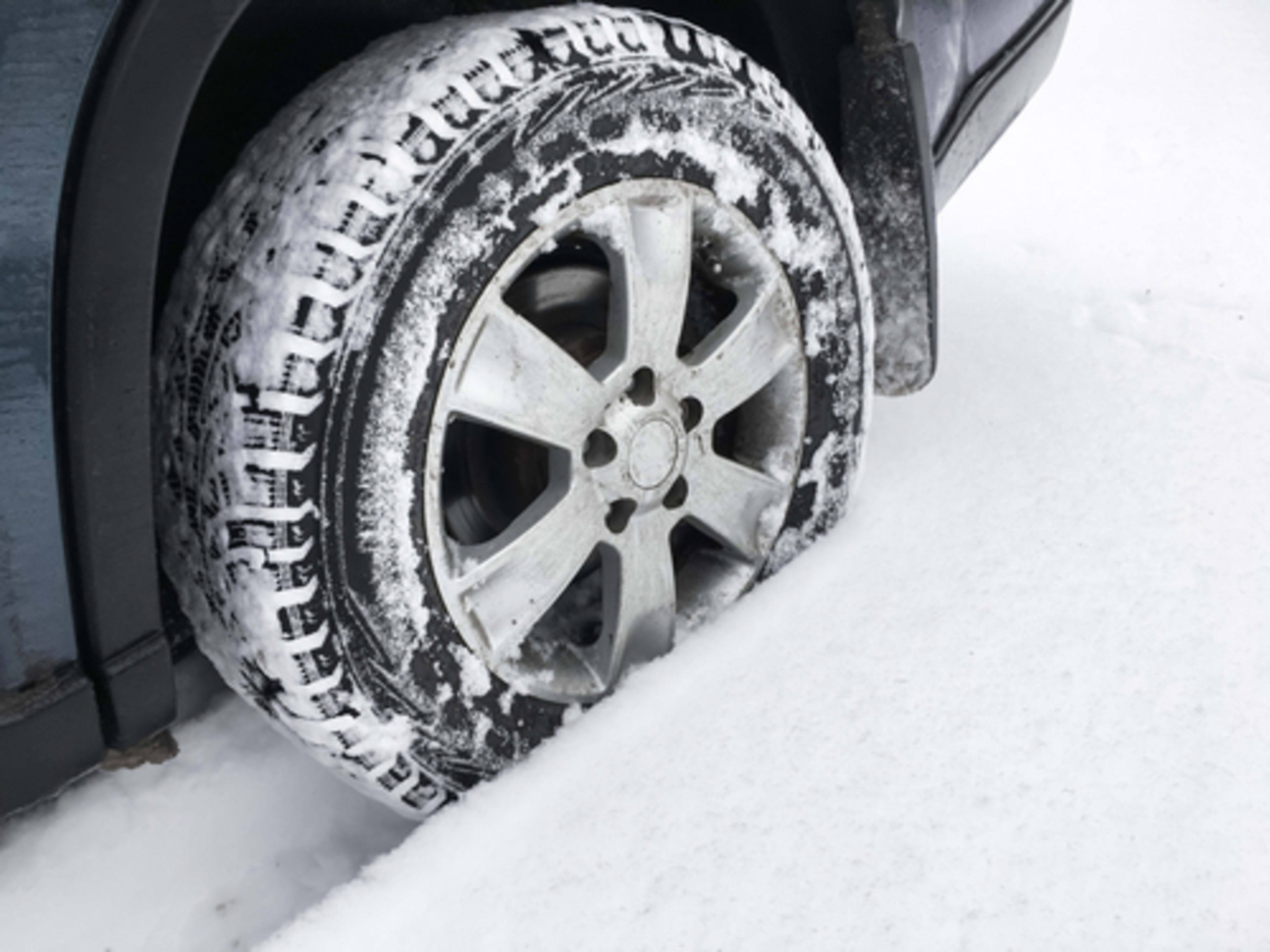 A snow covered winter tire and rim, driving through a few inches of snow.