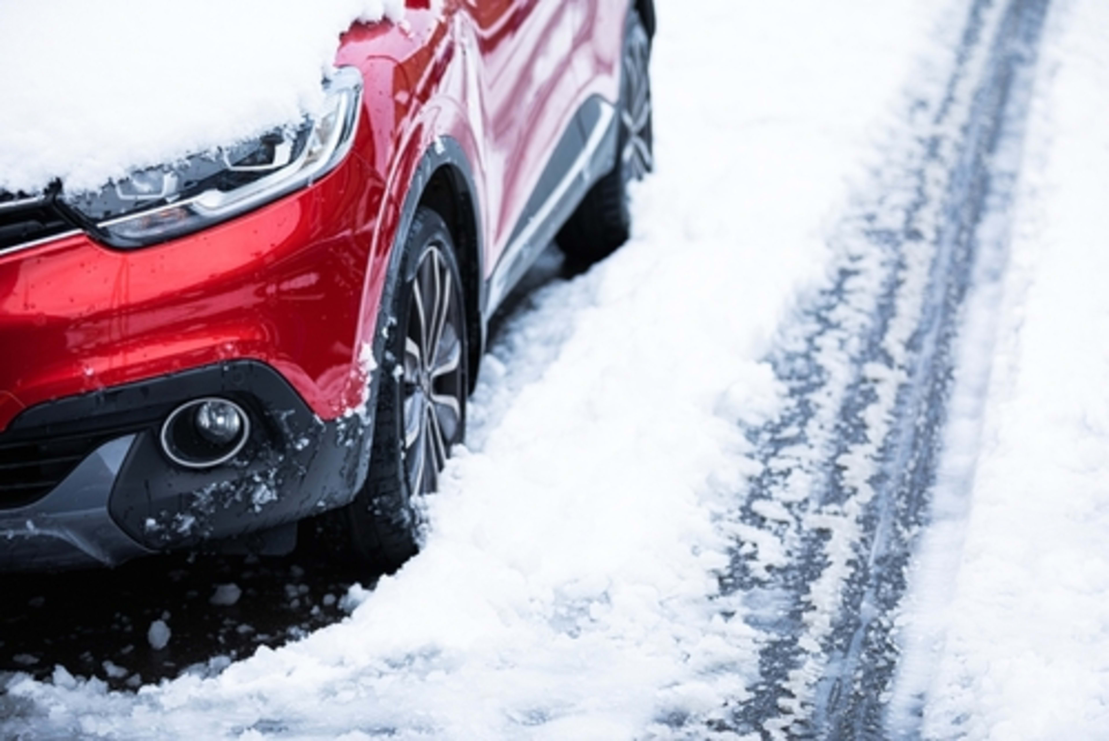 Red vehicle on the side of the road, covered in snow, showing a passing car's tire tread pattern in the snow.