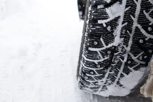 Close-up of a winter tire with studs driving on down a snowy road, leaving tread tracks behind.