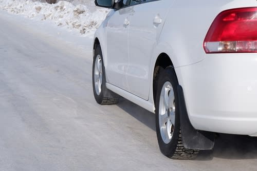 White passenger car driving safely on a snowy winter road.